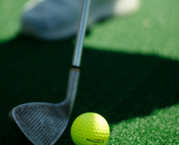 Close-up of golf ball and club on turf, symbolizing a sports legacy.