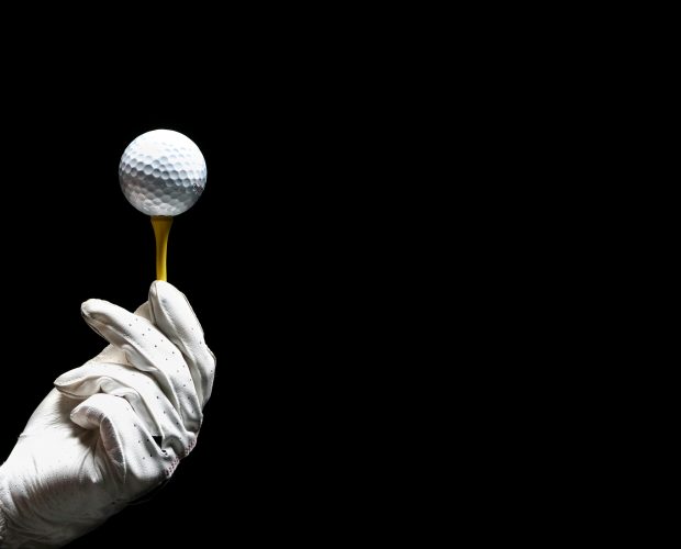 Golf glove holding ball on tee, prelude to a championship shot